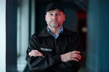 man in security uniform with arms crossed posing in a dimly lit environment representing authority and vigilance for safety